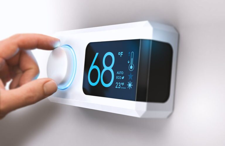 smart thermostat against a while wall with hand turning dial